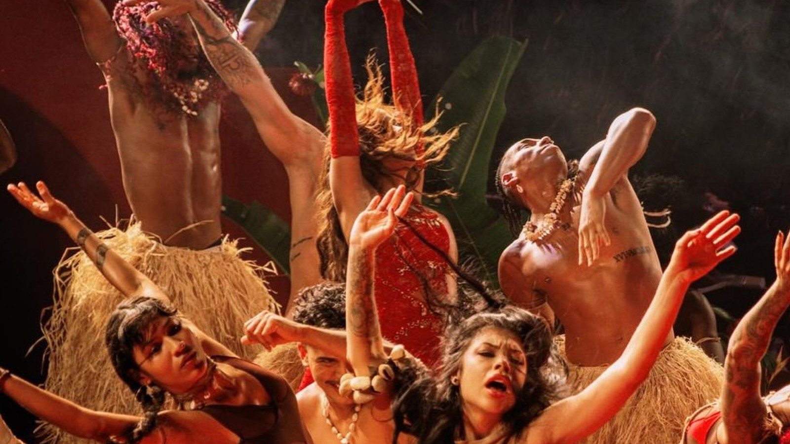 Anitta e bailarinos em coreografia no chao do palco sob luz vermelha