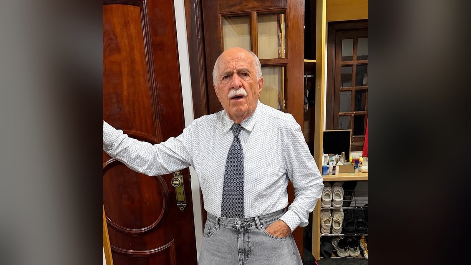 Ary Fontoura de camisa branca e gravata, com calça larguíssima, na porta de casa