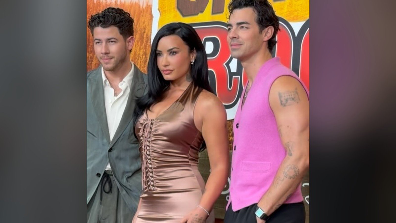 Demi Lovato posa ao lado de tres homens diante de um painel colorido