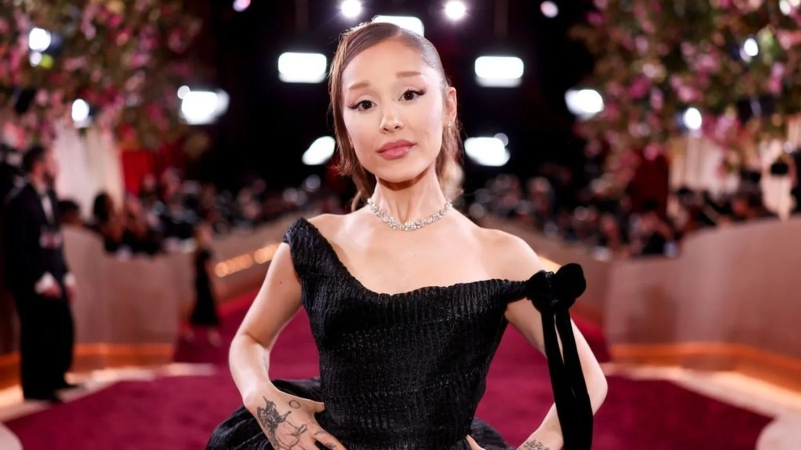 Ariana Grande de vestido preto posa em tapete vermelho cercada de flashes