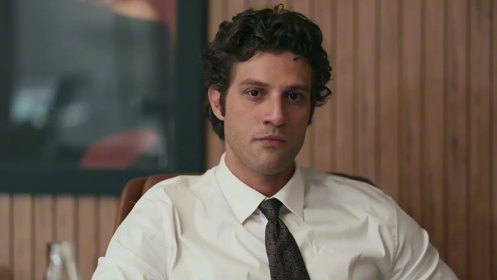 Chay Suede como Pedro, de camisa branca e gravata, sentado no escritório de advocacia em cena de Quem Ama Cuida