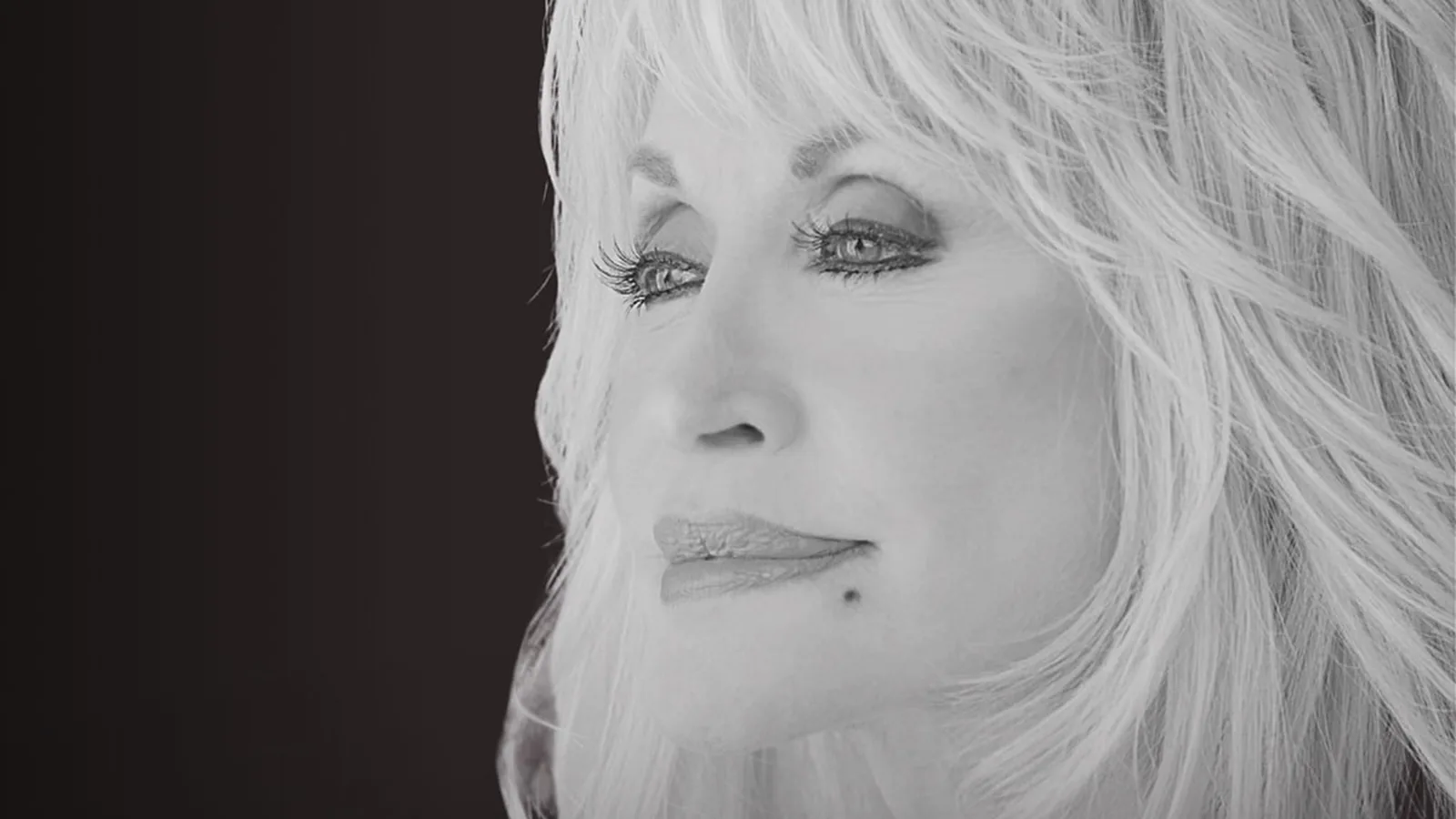 Retrato em preto e branco de Dolly Parton, de cabelo loiro volumoso, olhando para o lado