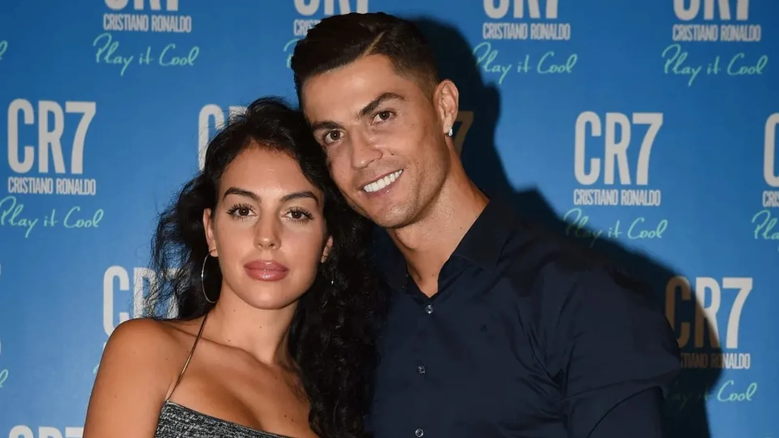 Georgina Rodríguez e Cristiano Ronaldo posando juntos diante de um painel com a marca CR7