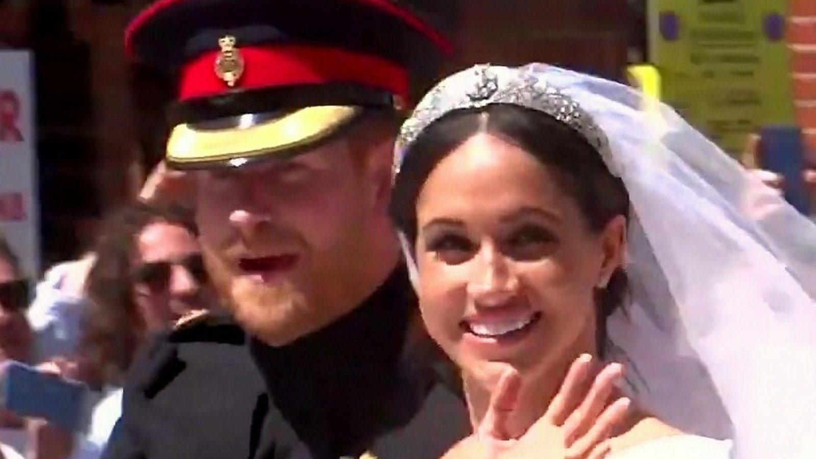 Harry de uniforme militar e Meghan de vestido de noiva e tiara acenam na carruagem do casamento em 2018