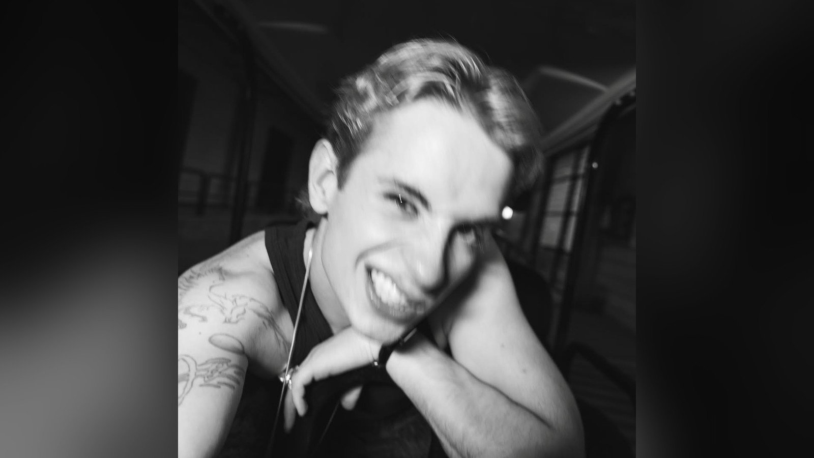 Juliano Floss em foto em preto e branco, sorrindo com a mao apoiando o rosto