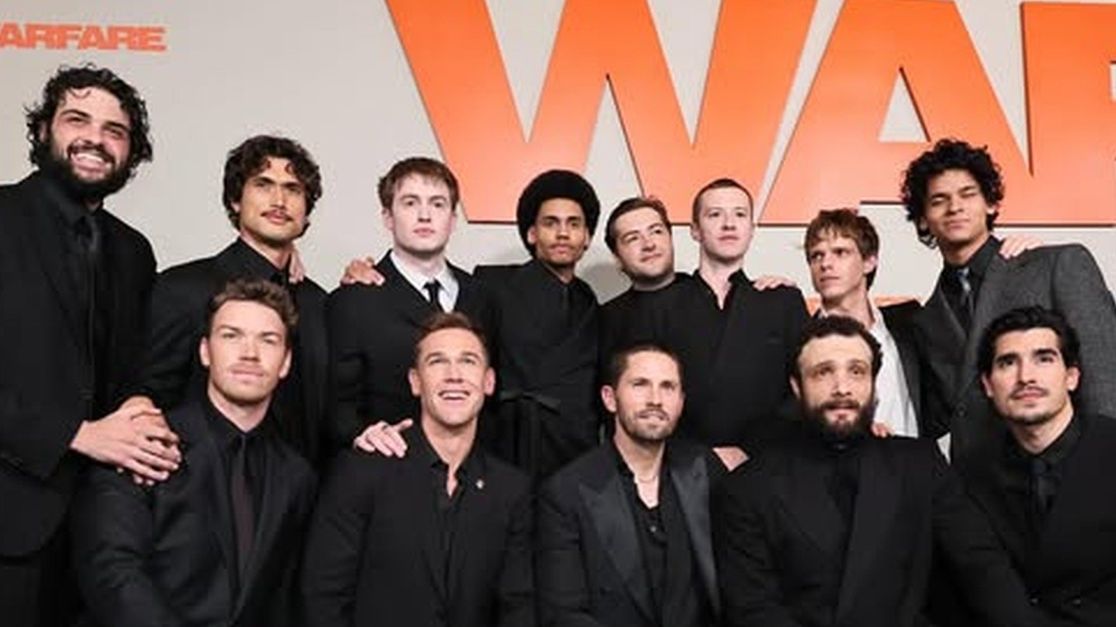 Elenco do filme Warfare posado diante do painel de divulgação, com Kit Connor entre os atores