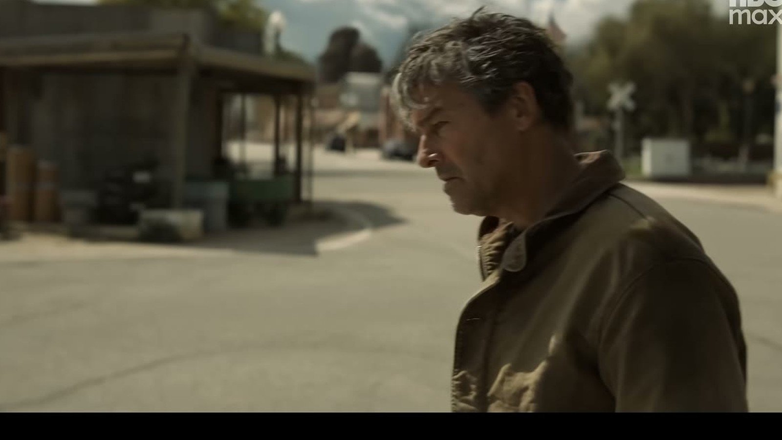 Kyle Chandler como Hal Jordan caminha num posto de estrada em cena diurna da serie