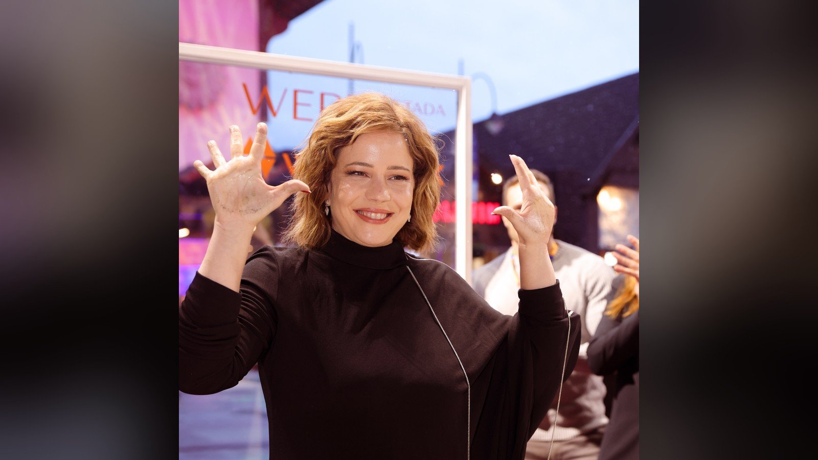 Leandra Leal sorrindo com as maos levantadas, de gola alta escura, em evento