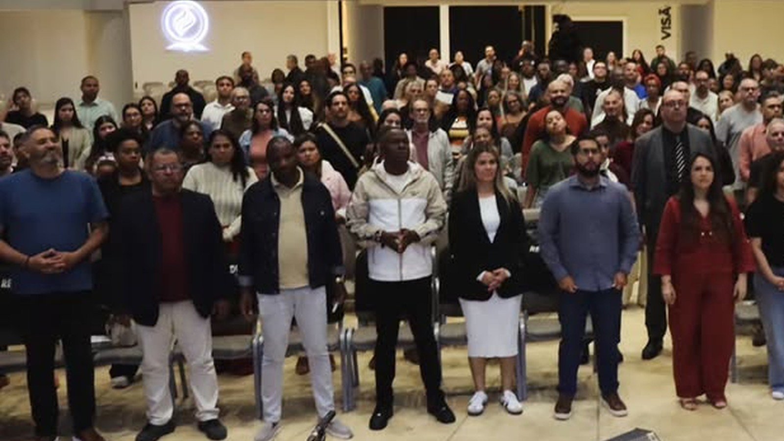 Marquinhos Menezes ao microfone diante de uma igreja lotada, com fieis em pe