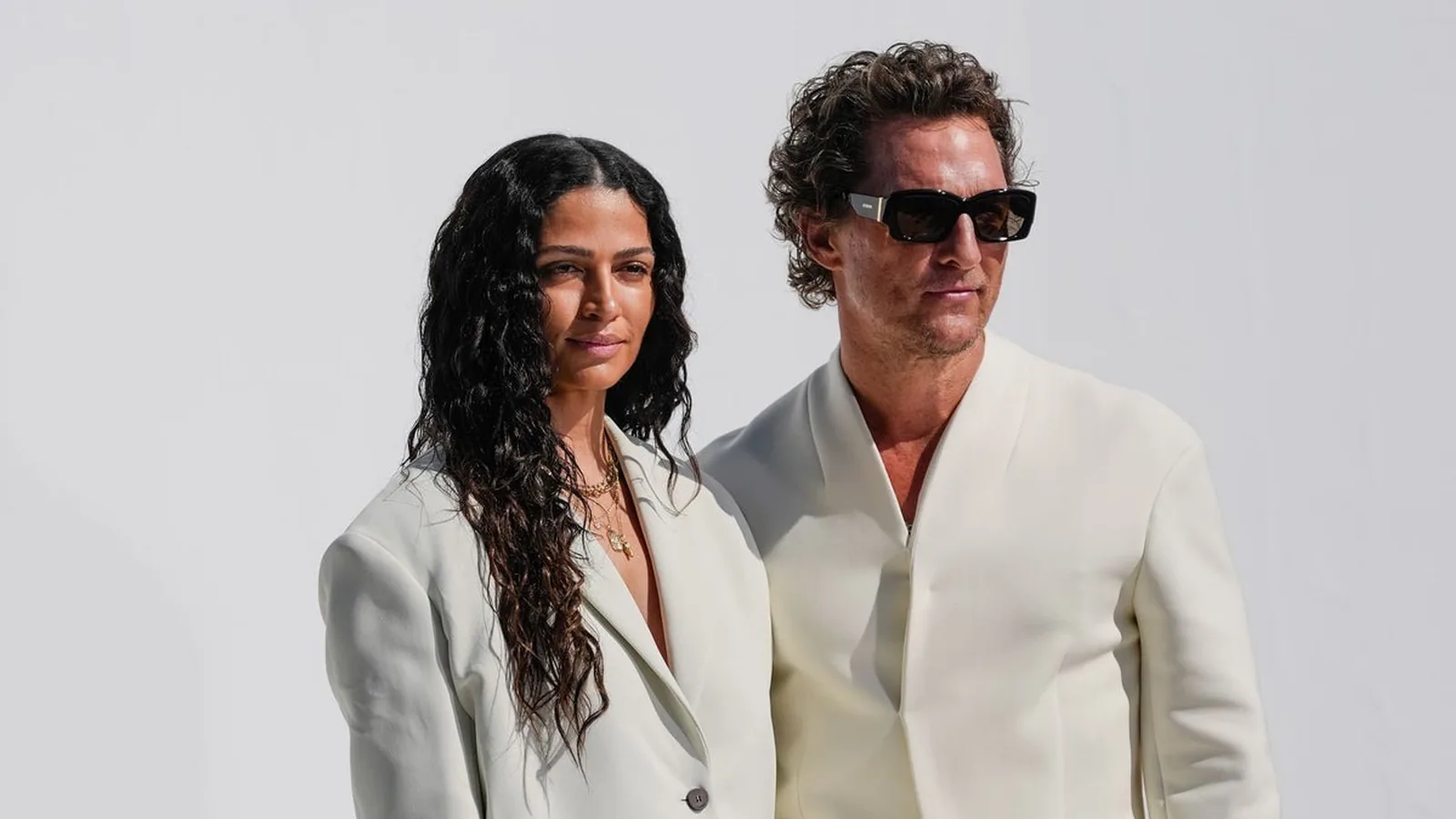 Camila Alves e Matthew McConaughey posando juntos, ela de terno claro e ele de blazer branco e óculos escuros