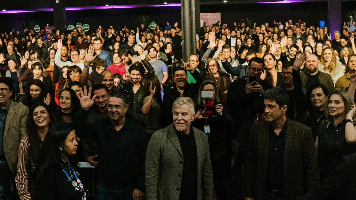 Miguel Falabella, de blazer cinza e cabelo branco, sorri no meio da plateia de uma de suas palestras
