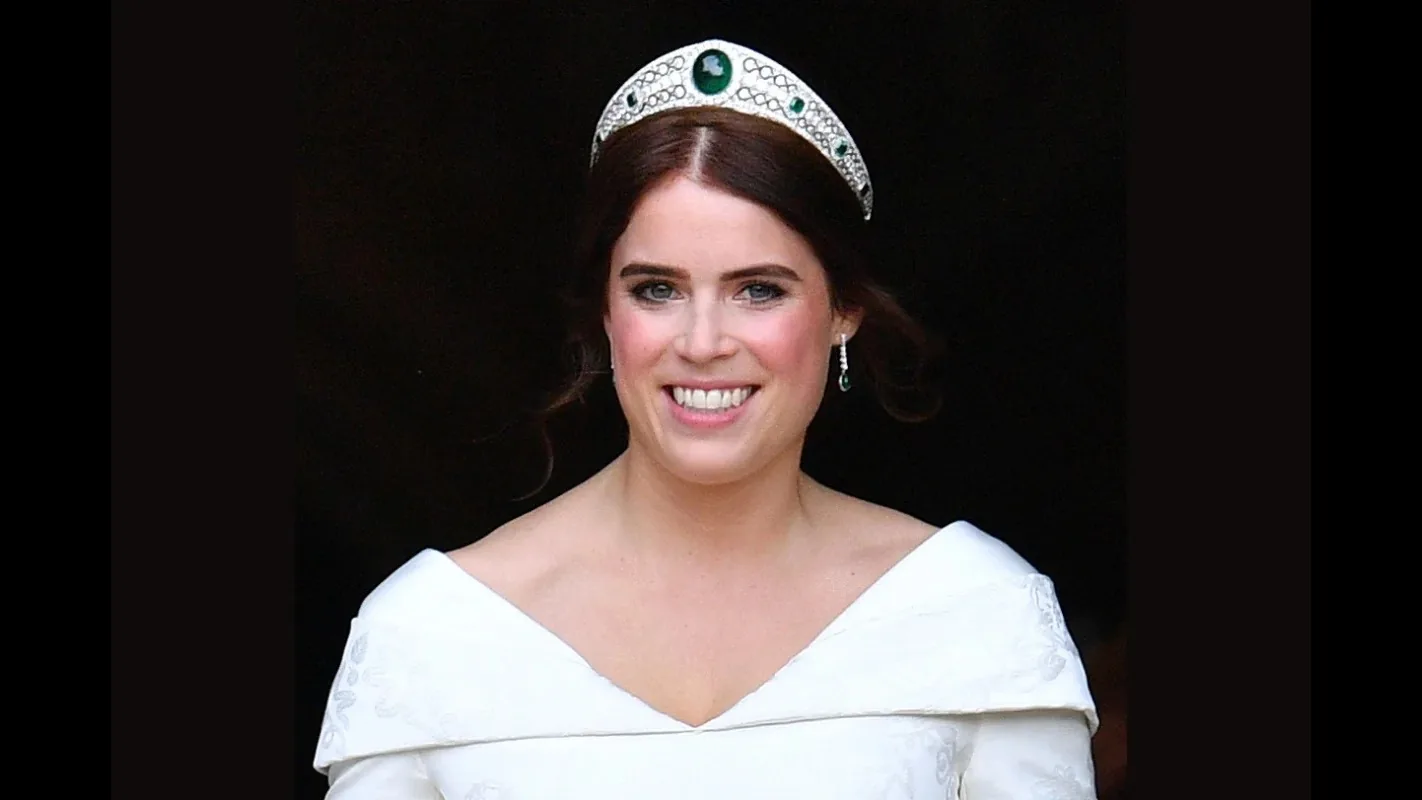 Princesa Eugenie de tiara e vestido branco, sorrindo, em fundo escuro