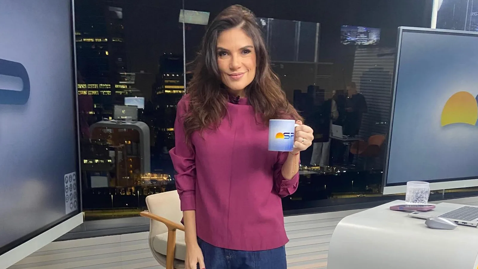 Sabina Simonato, de blusa vinho, segura uma caneca no cenário do Bom Dia São Paulo