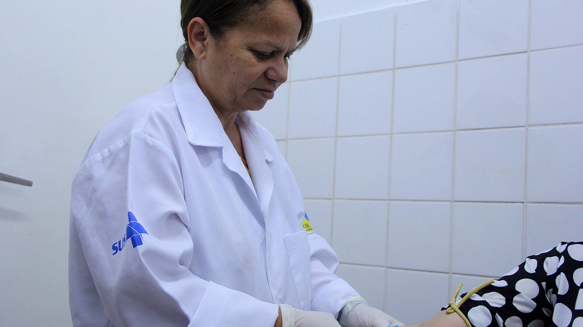 Profissional de saúde faz punção venosa no braço de uma paciente em unidade da rede pública
