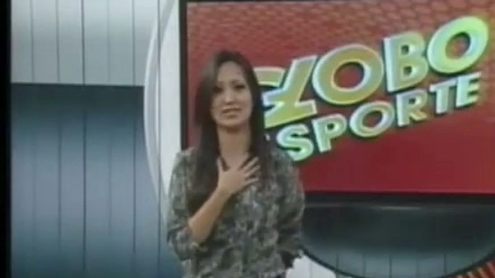 Thalita Tavares, de blusa estampada, com a mão no peito no cenário do Globo Esporte Tocantins