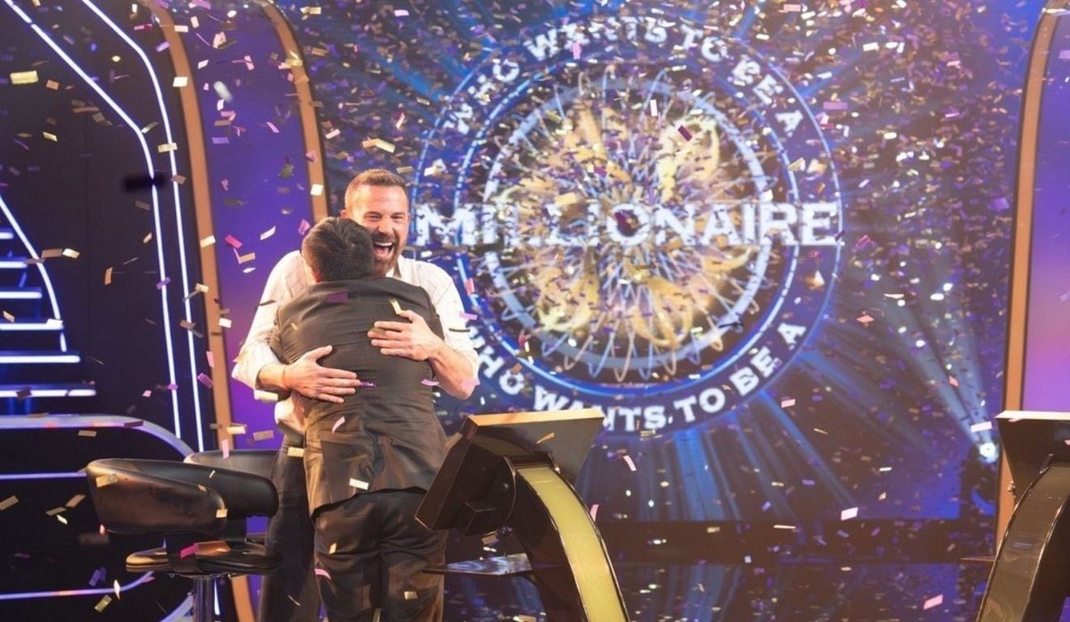 Ben Affleck abraça o parceiro de dupla no palco do Quem Quer Ser um Milionário, com confete caindo
