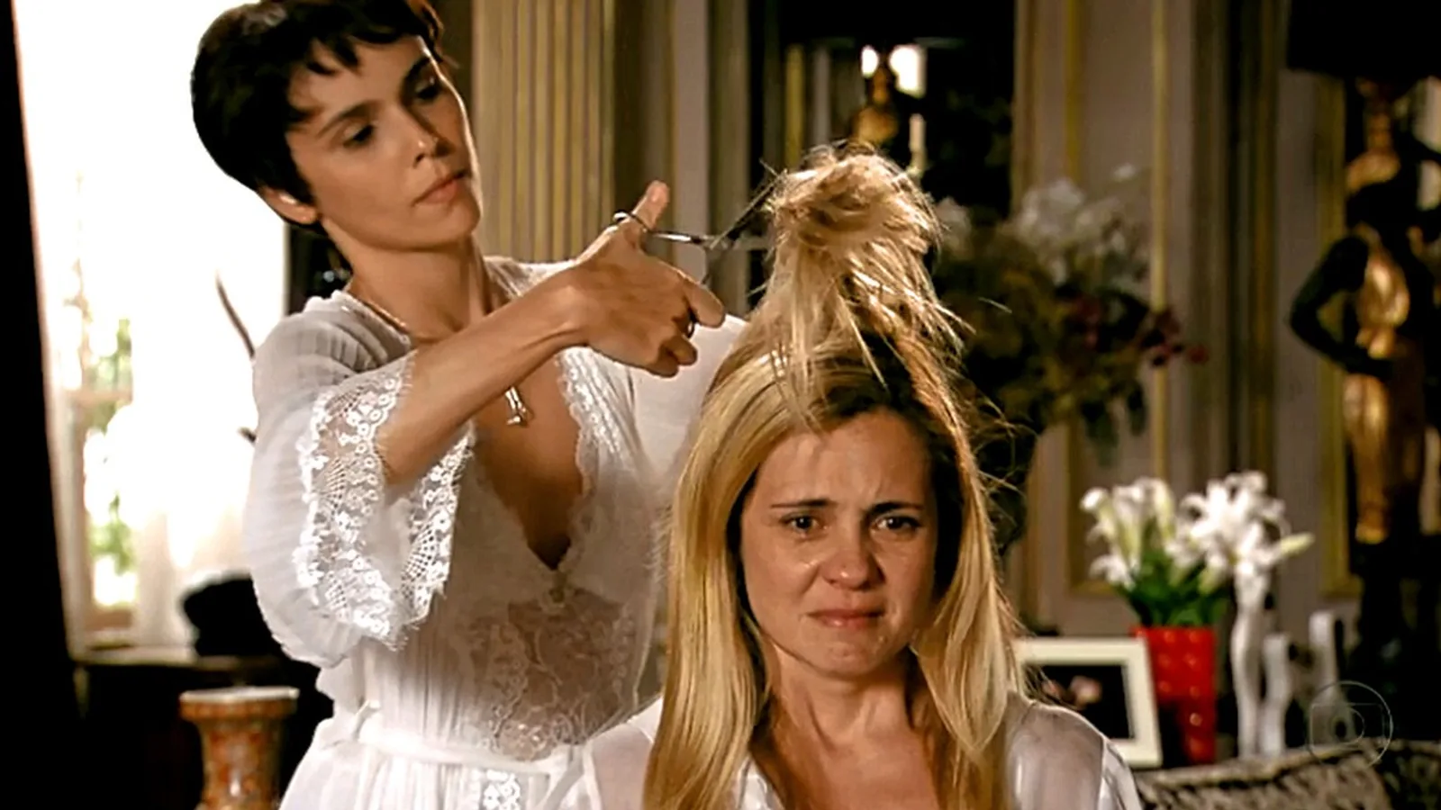 Nina, de cabelo curto escuro, corta o cabelo de Carminha com uma tesoura enquanto a vilã chora, em cena de Avenida Brasil