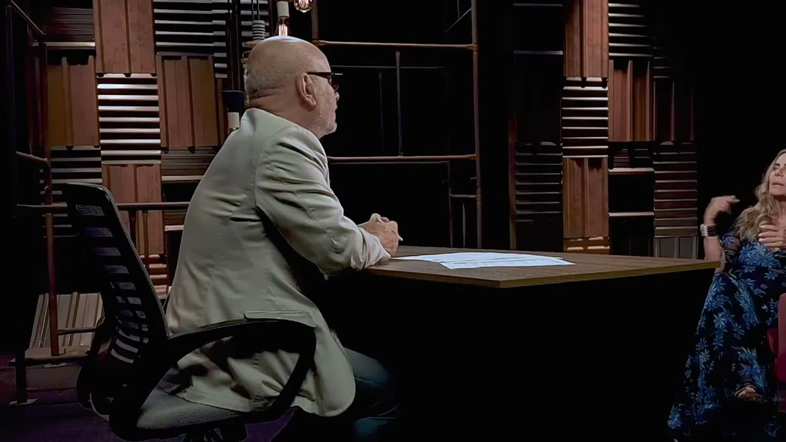 Bruna Lombardi sentada em poltrona vermelha durante entrevista de televisão, com o entrevistador à mesa