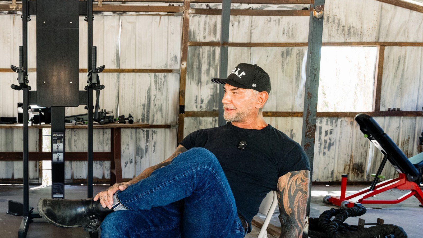 Dave Bautista sentado num banco de academia, de bone e camiseta preta