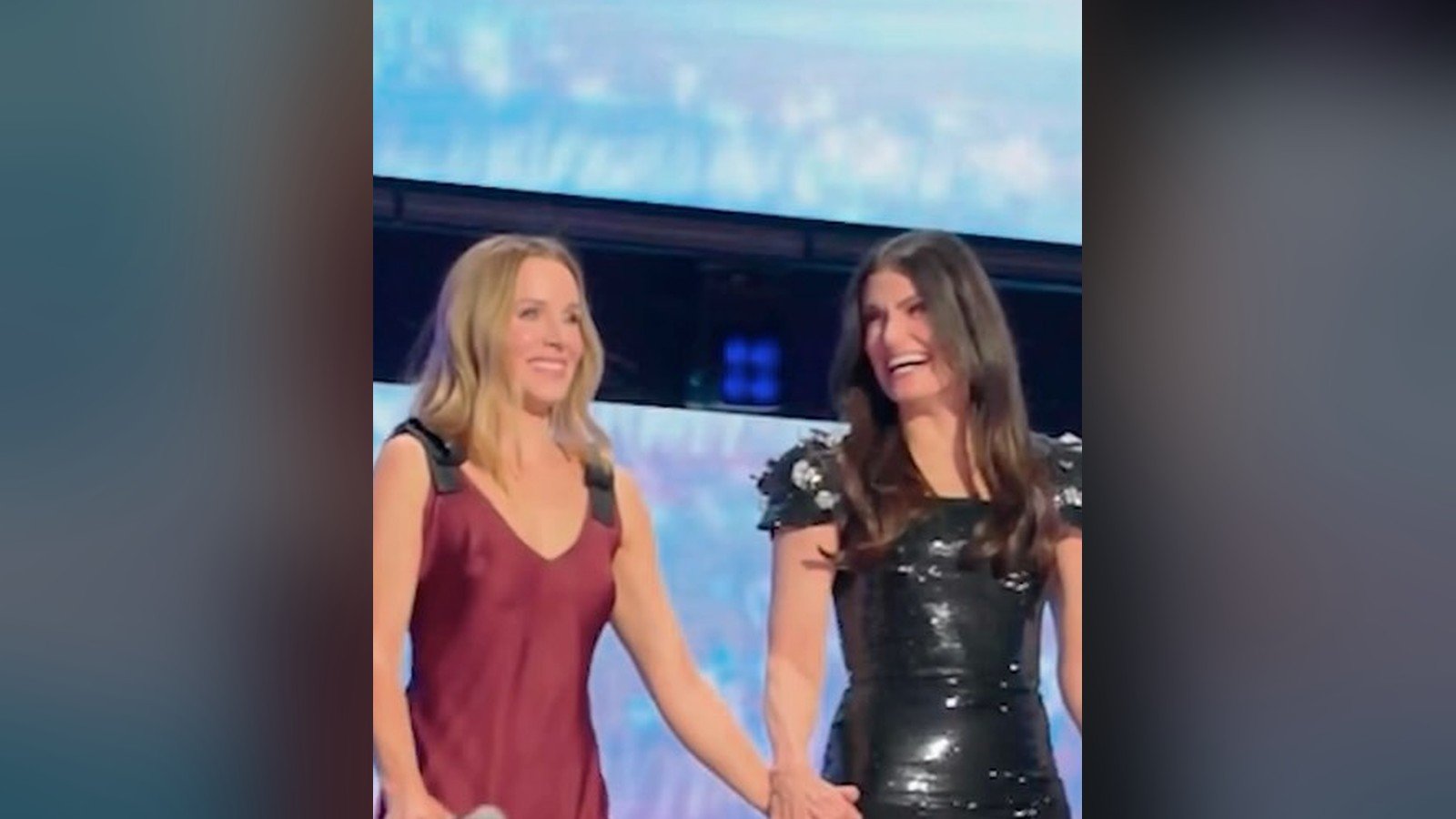 Kristen Bell e Idina Menzel de maos dadas no palco da D23, sorrindo