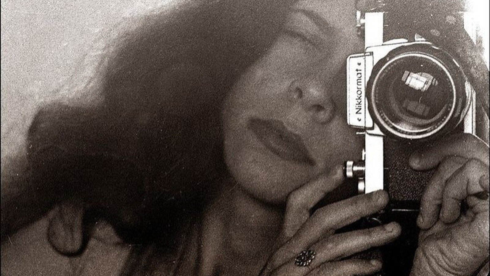 Gal Costa em foto em preto e branco, segurando uma camera fotografica junto ao rosto