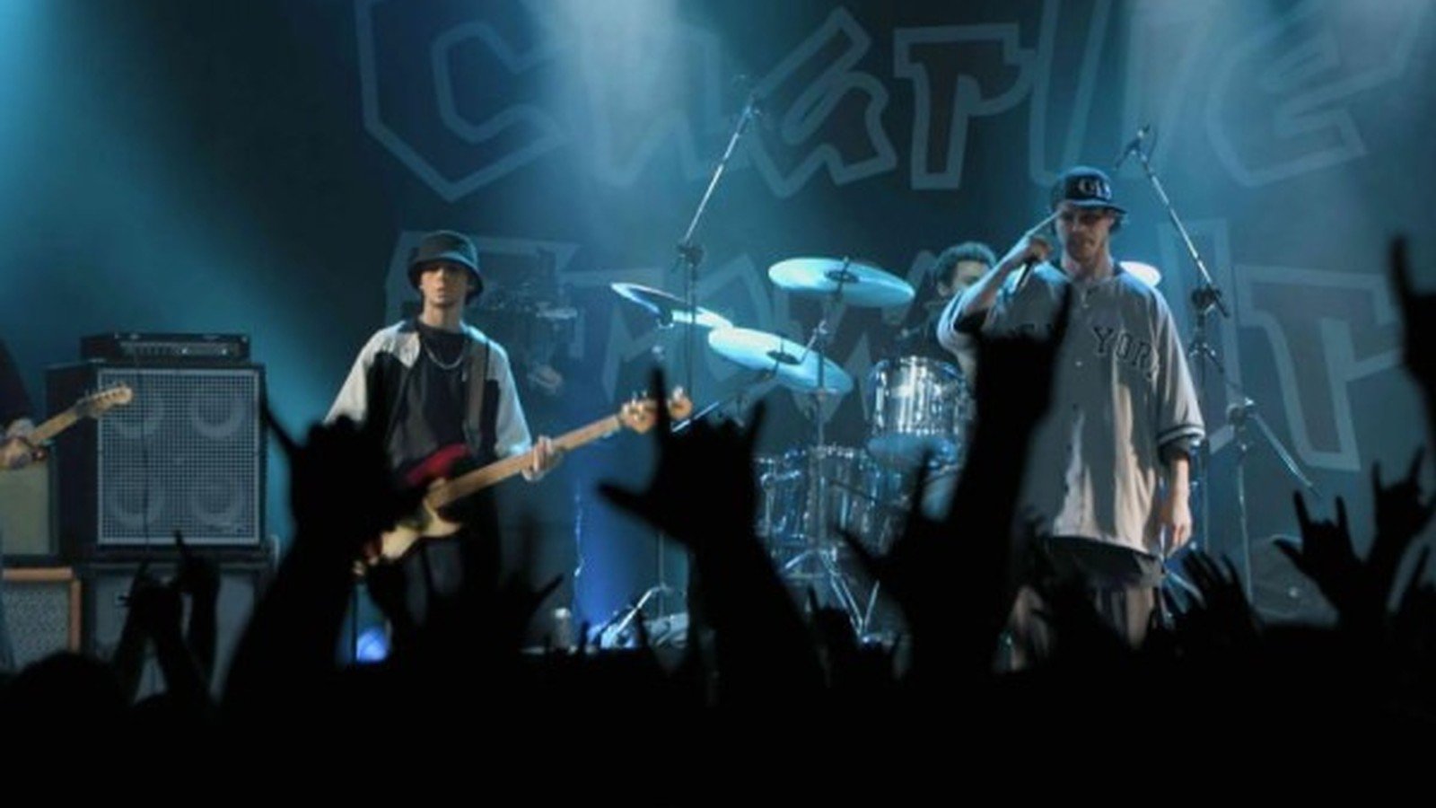 Cena de show do filme, banda no palco com plateia de maos levantadas