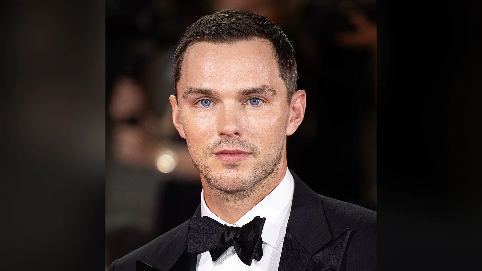 Nicholas Hoult de cabelo loiro, terno e camisa listrada, em evento