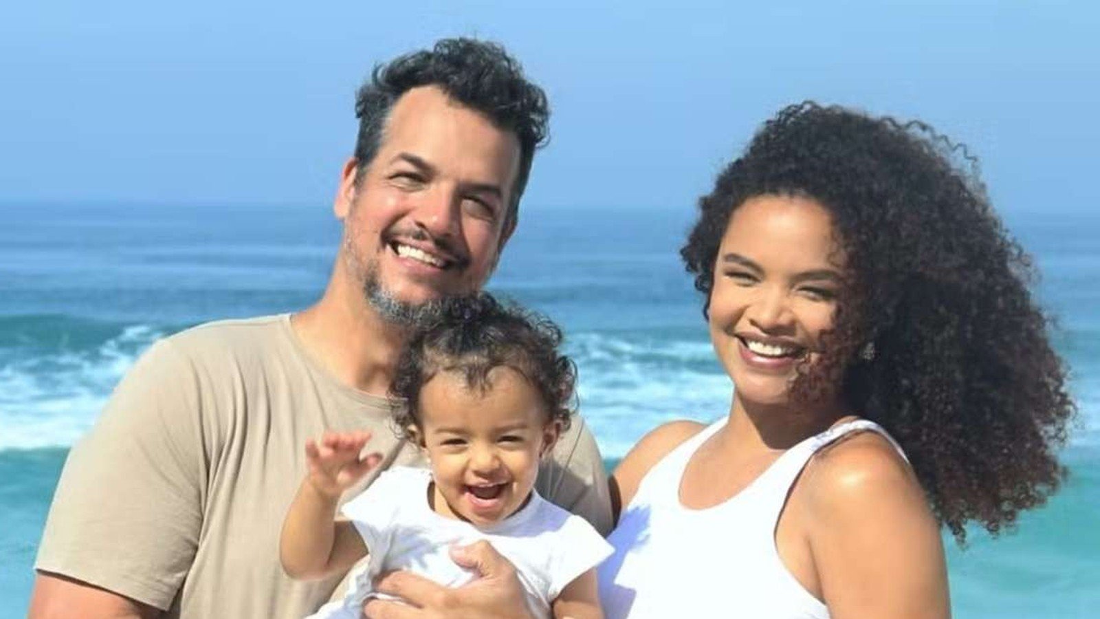 Lucy Ramos, Thiago Luciano e a filha Kyara sorrindo na praia