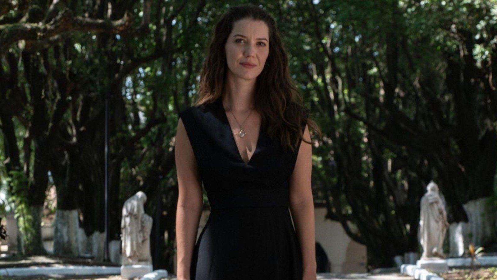 Nathalia Dill como Francesca, de vestido preto, entre estatuas e arvores do cemiterio