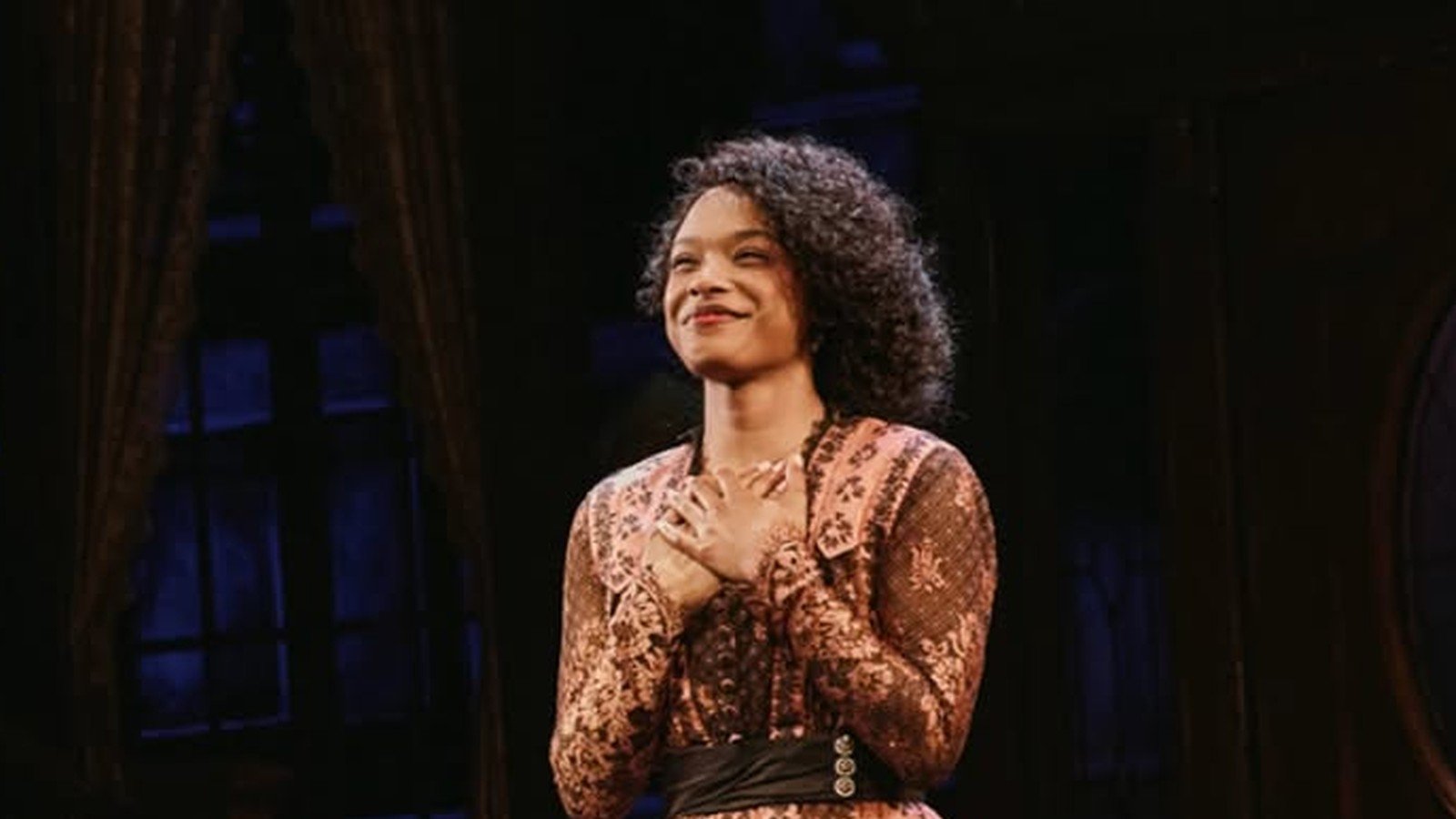 Maya Boyd em cena no palco, de vestido estampado, sob luz de espetaculo