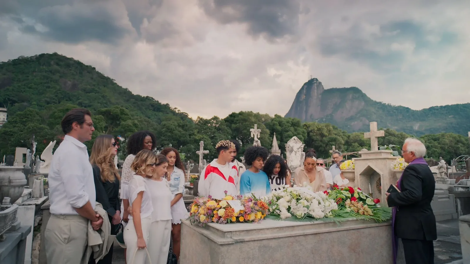Cena de velório em cemitério do Rio de Janeiro, com o Corcovado ao fundo e o caixão coberto de flores