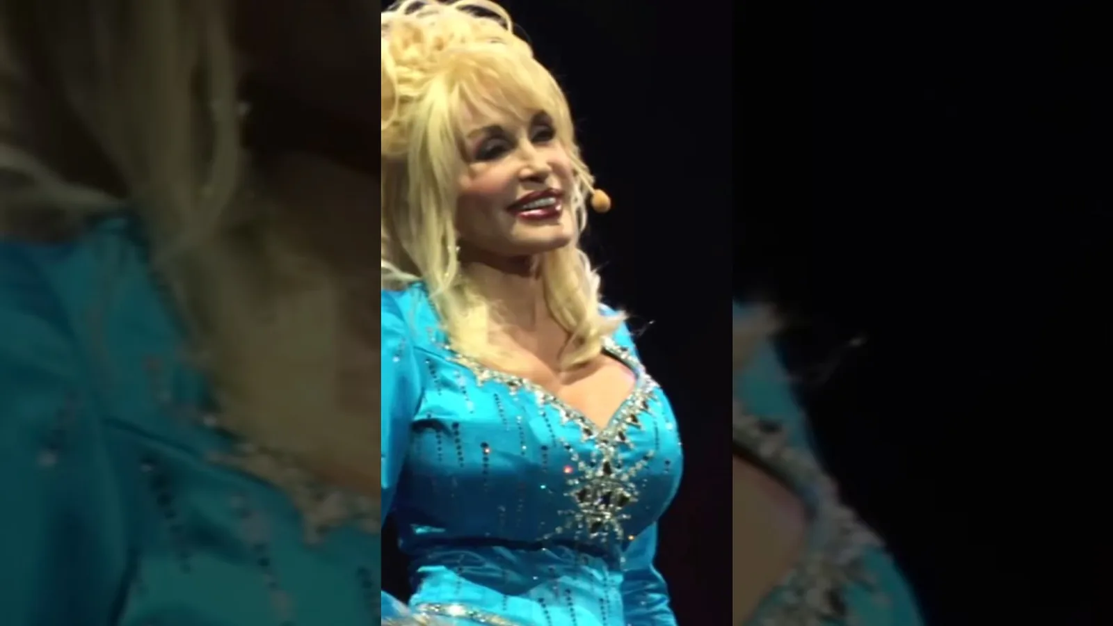 Dolly Parton, de vestido azul brilhante e cabelo loiro volumoso, canta no palco diante da plateia