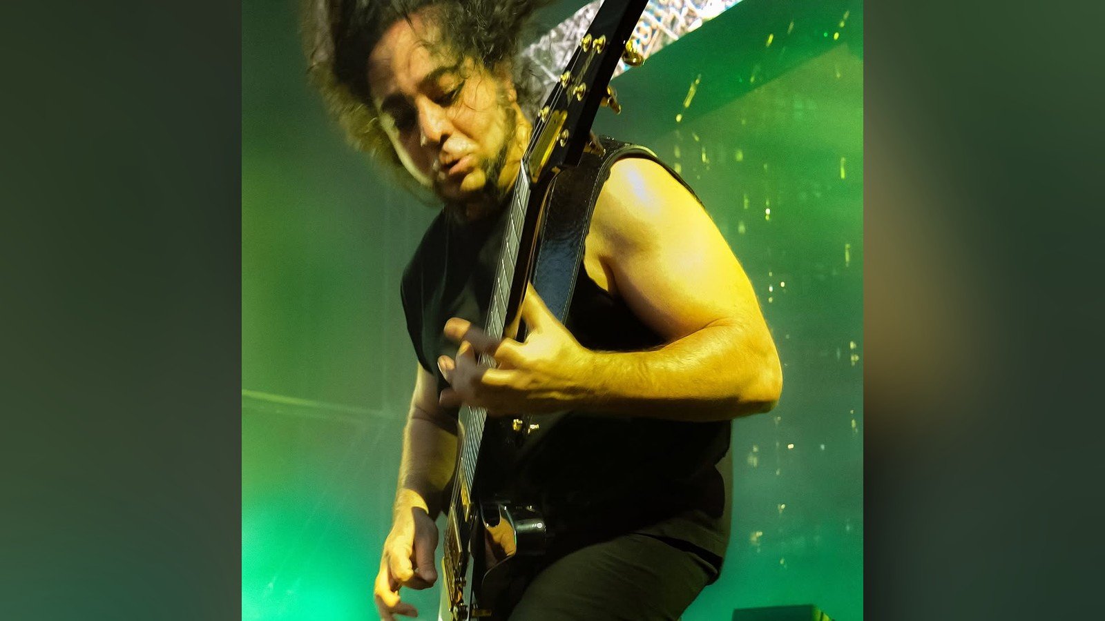 Guitarrista do System of a Down toca de perfil sob luz verde no palco