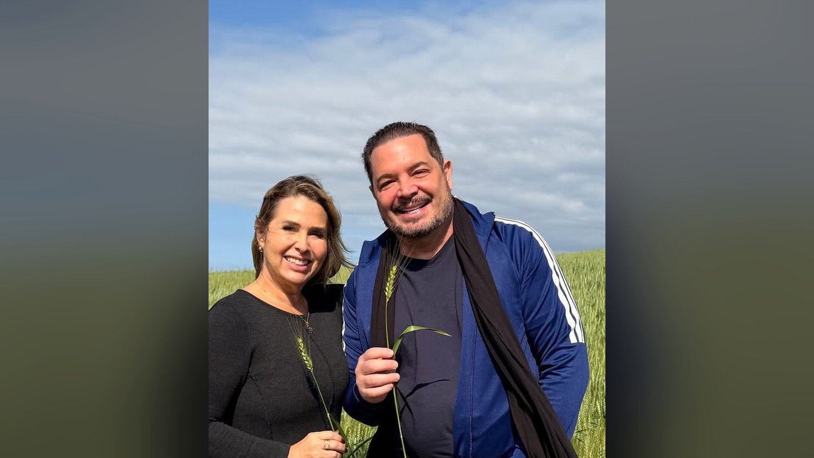 Andréa Sorvetão e o cantor Conrado de pé em uma plantação, durante viagem de trabalho ao Paraná