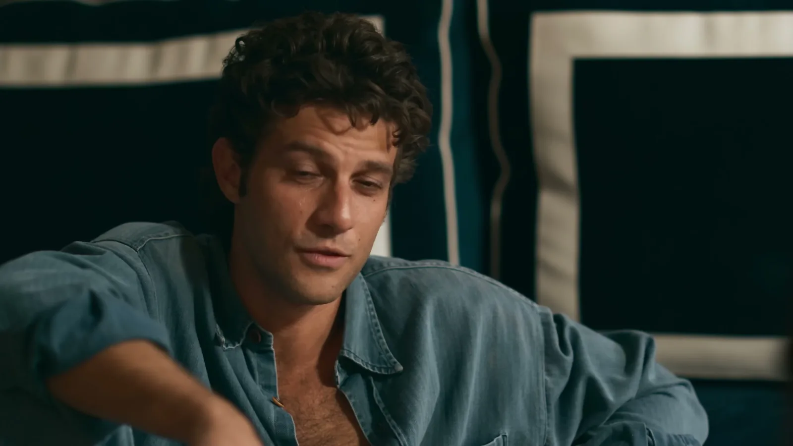 Chay Suede como Pedro, de camisa jeans aberta, olhando para baixo em cena noturna de Quem Ama Cuida