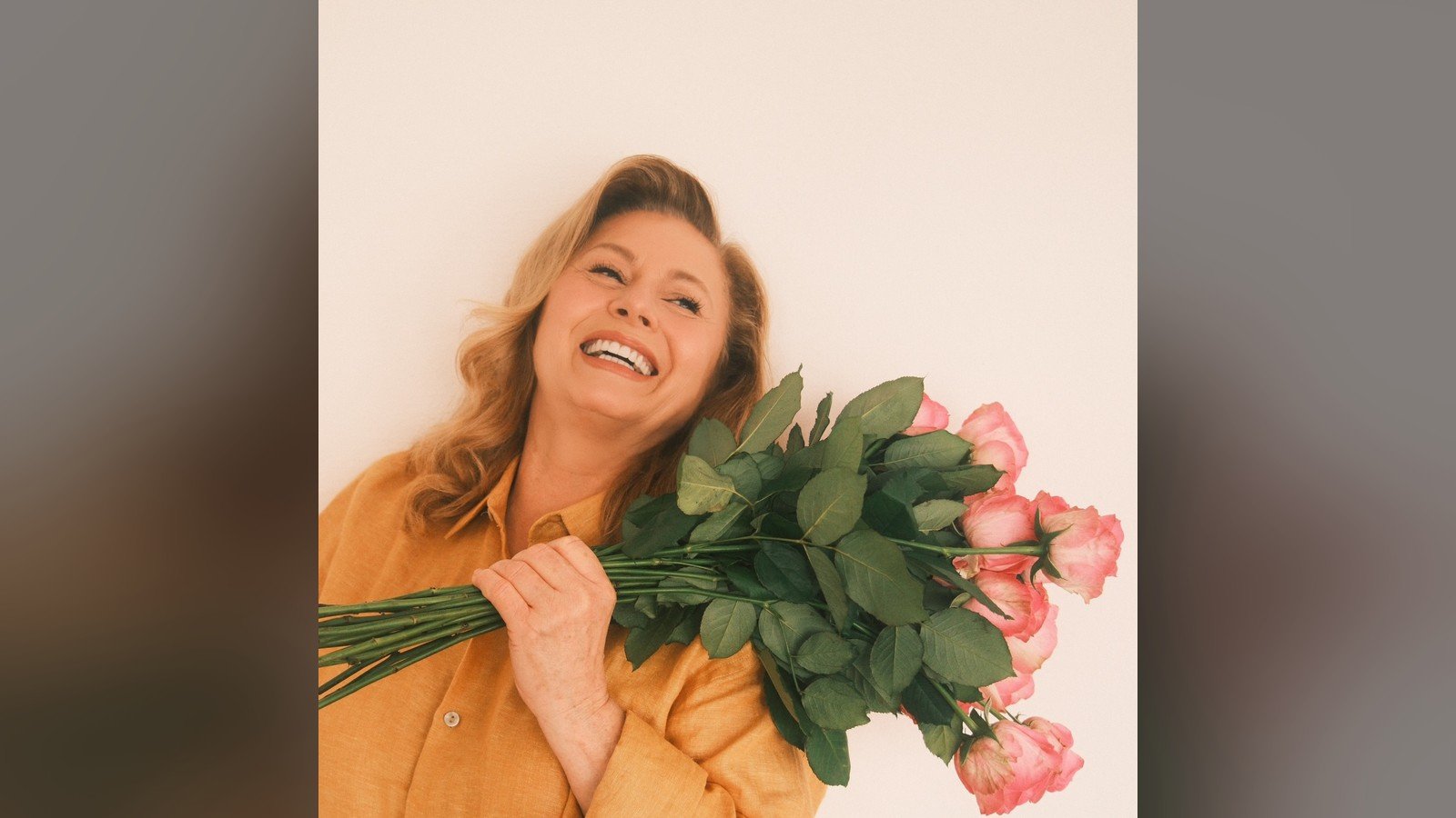 Vera Fischer de camisa laranja, sorrindo, segurando um buquê de rosas