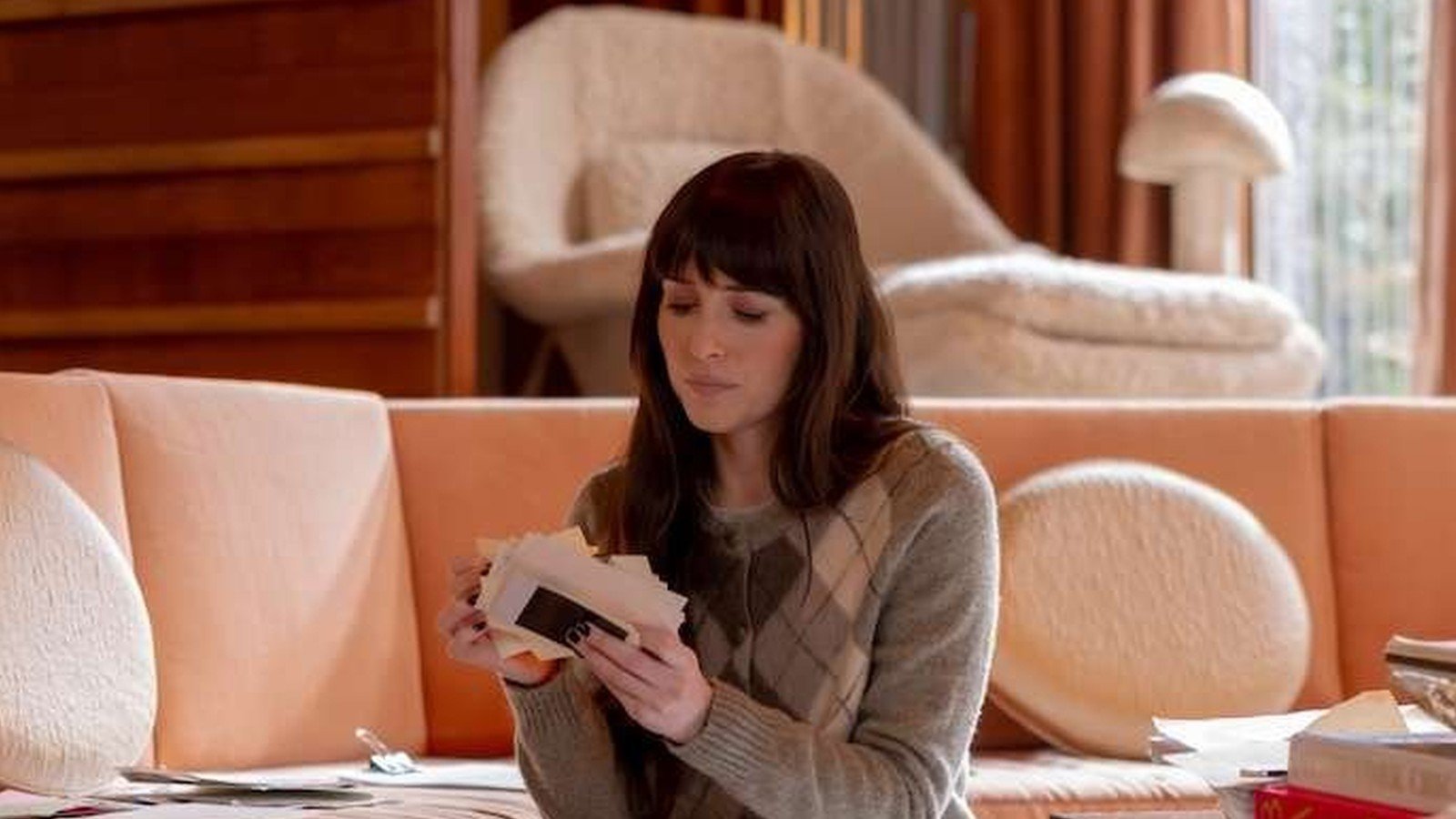 Dakota Johnson sentada no chão da sala, cercada de papéis, lendo folhas do manuscrito