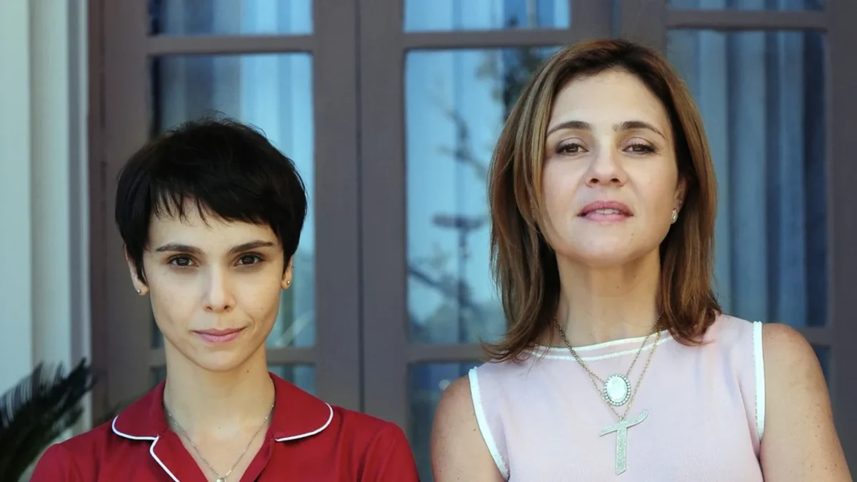 Débora Falabella, como Nina, e Adriana Esteves, como Carminha, lado a lado diante de uma janela em cena de Avenida Brasil