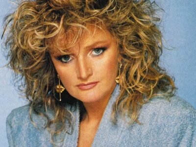 Retrato de Bonnie Tyler nos anos 1980, de cabelos loiros cacheados e blusa azul-clara