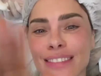 Carolina Dieckmann sorrindo, de touca cirúrgica, deitada na maca da clínica