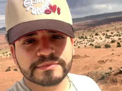 César Gastélum de boné bege, barba escura, em selfie ao ar livre