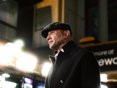 Dave Bautista de boina e sobretudo preto, de perfil, numa pre-estreia em Londres