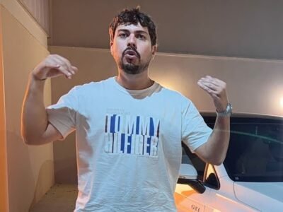 Eduardo Razuk, de camiseta clara, gesticula ao lado de um Volkswagen Golf branco num galpao com outros carros