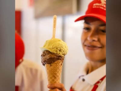 Atendente de boné vermelho da Gelateria Miracolo segura uma casquinha com gelato de chocolate e pistache