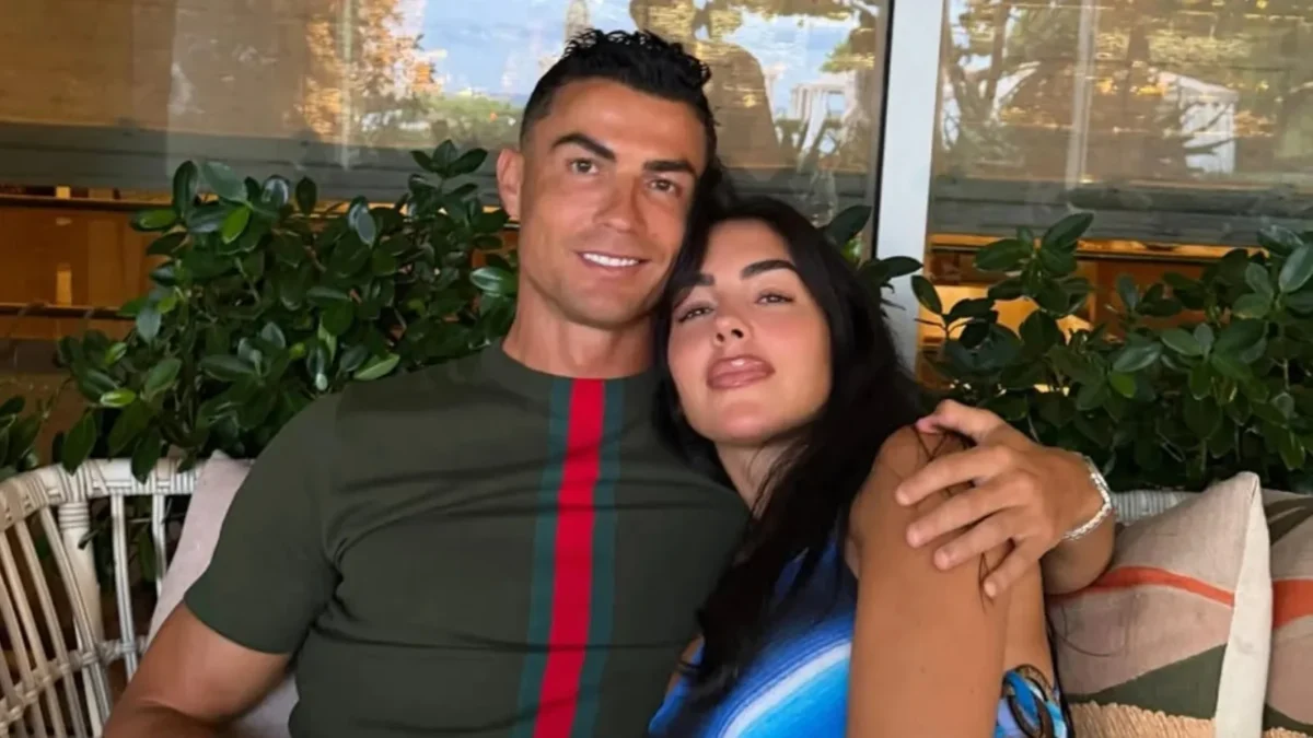 Cristiano Ronaldo abraçando Georgina Rodríguez, os dois sentados e sorrindo, em ambiente com plantas ao fundo