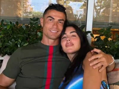 Cristiano Ronaldo abraçando Georgina Rodríguez, os dois sentados e sorrindo, em ambiente com plantas ao fundo