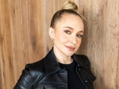 Hayden Panettiere de jaqueta de couro preta e cabelo preso, diante de uma parede de madeira