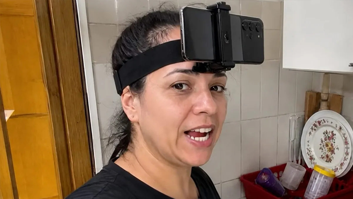Mulher com celular preso à testa por faixa de cabeça, numa cozinha, gravando tarefa doméstica