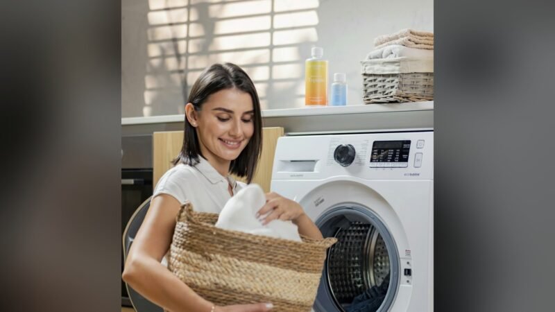 Mulher segurando um cesto de roupa suja em frente à máquina de lavar, em casa