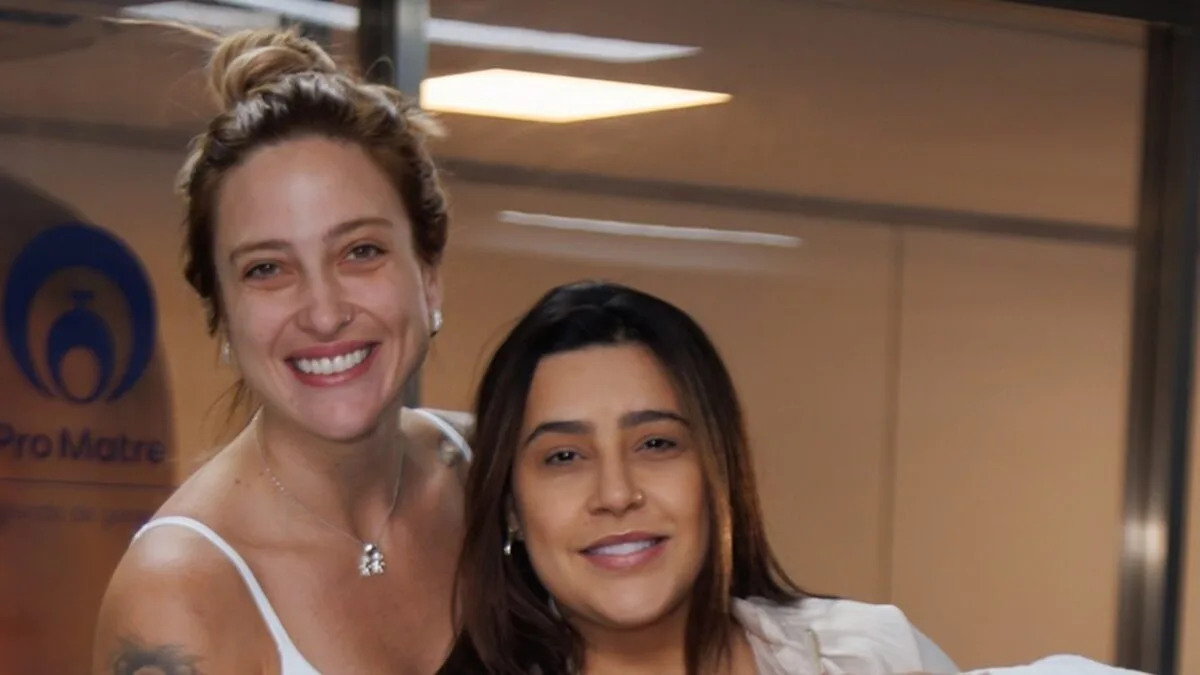 Lauana Prado e Tati Dias sorrindo na saída da maternidade, com o logo do Pro Matre ao fundo